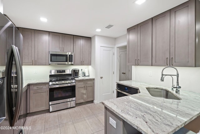 kitchen featuring sink, light stone countertops, appliances with stainless steel finishes, and light tile patterned flooring