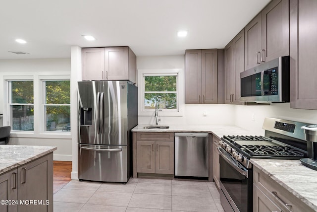 kitchen with light stone counters, stainless steel appliances, sink, and light tile patterned floors