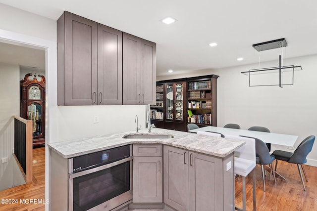 kitchen featuring kitchen peninsula, sink, stainless steel oven, light stone countertops, and light hardwood / wood-style floors