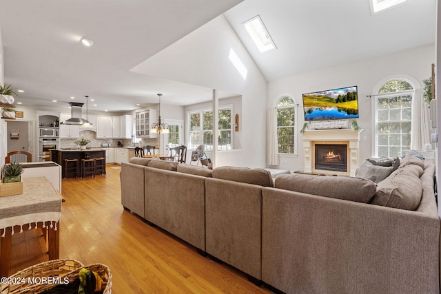 living room featuring vaulted ceiling, plenty of natural light, a notable chandelier, and light wood-type flooring