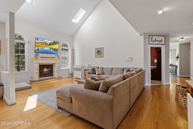 living room featuring light wood-type flooring, high vaulted ceiling, and a skylight