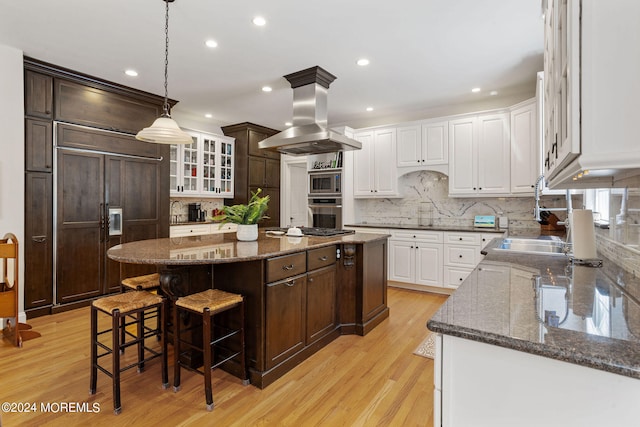 kitchen with a center island, built in appliances, light hardwood / wood-style floors, white cabinetry, and island exhaust hood