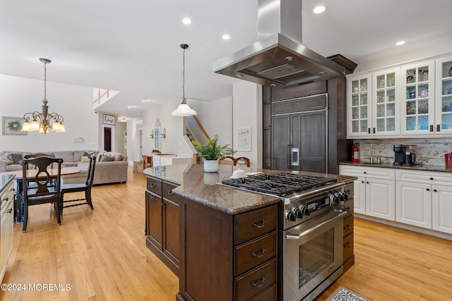 kitchen with high end appliances, white cabinets, decorative backsplash, light wood-type flooring, and island range hood