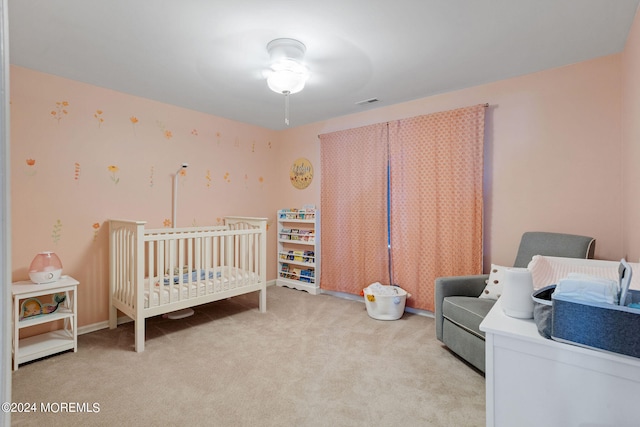 bedroom featuring a crib, light carpet, and ceiling fan