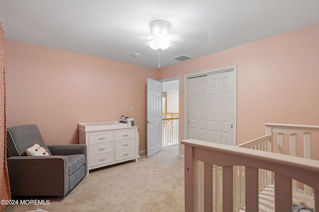 bedroom featuring light carpet, a nursery area, a closet, and ceiling fan