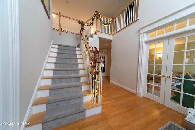 staircase featuring french doors, a towering ceiling, and wood-type flooring