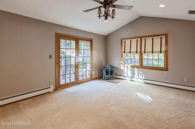 empty room featuring lofted ceiling, ceiling fan, a wood stove, a baseboard heating unit, and light colored carpet