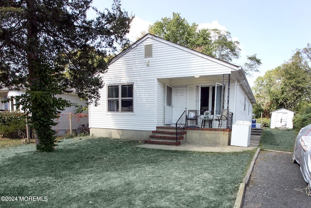 bungalow featuring a front yard, a porch, and a storage unit