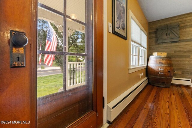 doorway to outside with wood-type flooring, a baseboard radiator, and wood walls