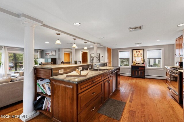 kitchen featuring a large island with sink, decorative columns, stainless steel appliances, and plenty of natural light