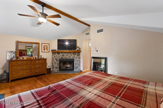 living room featuring vaulted ceiling with beams, a stone fireplace, hardwood / wood-style floors, and ceiling fan