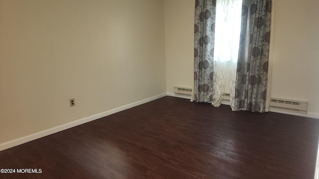 empty room with a baseboard heating unit and dark hardwood / wood-style flooring