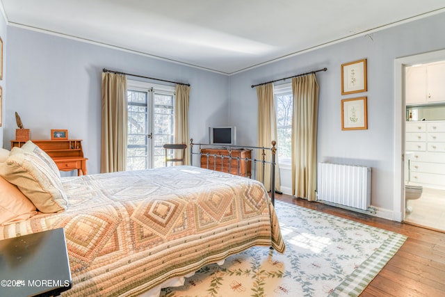 bedroom featuring radiator, connected bathroom, light hardwood / wood-style floors, and multiple windows