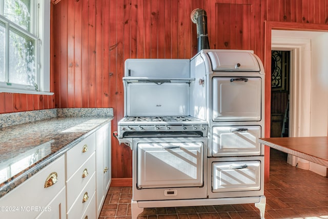 kitchen featuring washer / clothes dryer, wood walls, light stone counters, and white cabinets