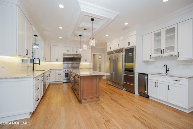 kitchen with high end appliances, white cabinets, light hardwood / wood-style floors, a kitchen island, and light stone counters