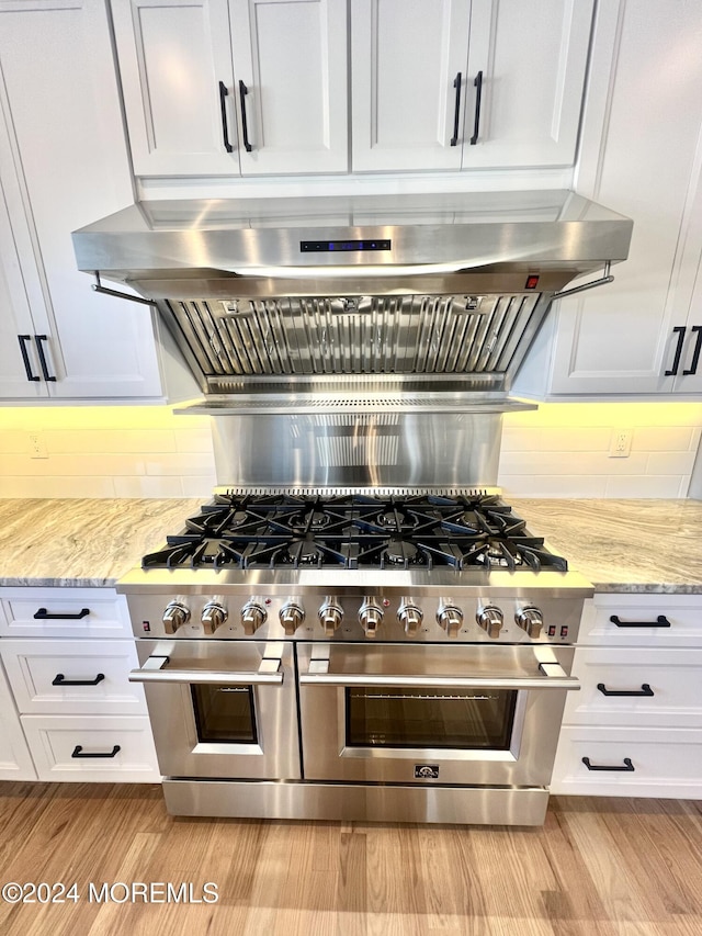 kitchen featuring white cabinetry, range with two ovens, light stone countertops, and tasteful backsplash