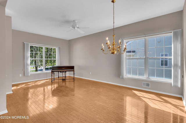 spare room with ceiling fan with notable chandelier and light wood-type flooring