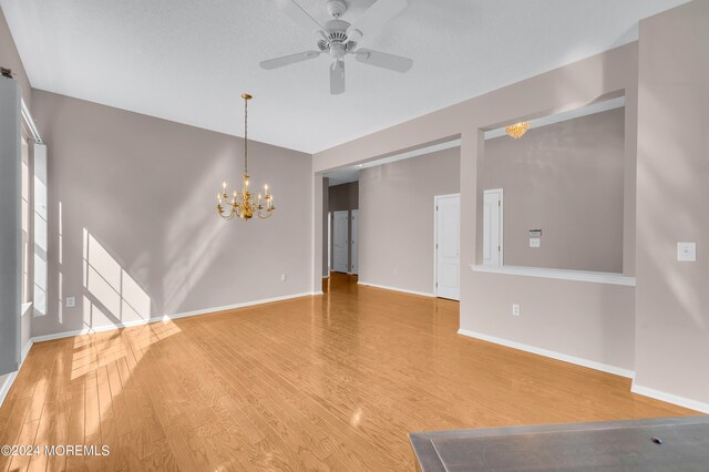 unfurnished room with ceiling fan with notable chandelier, wood-type flooring, and a textured ceiling