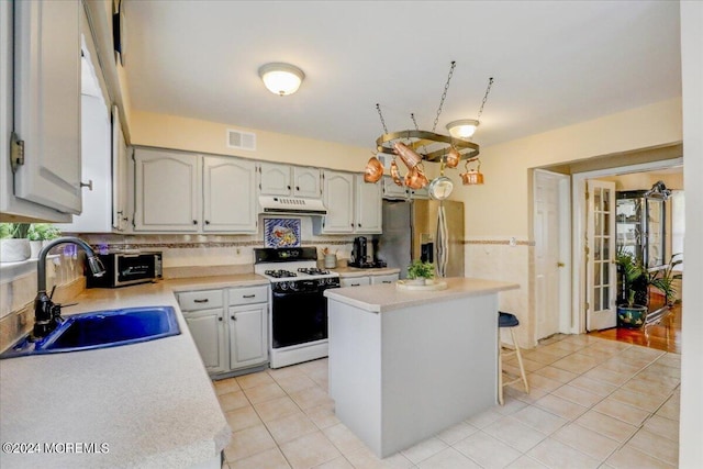 kitchen featuring sink, stainless steel refrigerator with ice dispenser, white range with gas stovetop, a center island, and a healthy amount of sunlight