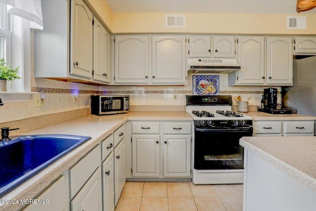 kitchen with white range, white cabinetry, light tile patterned flooring, and backsplash