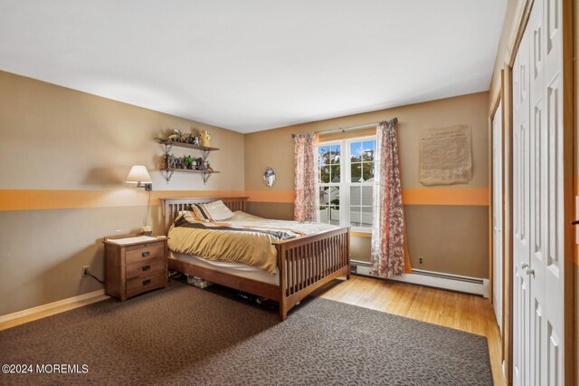 bedroom featuring a closet, a baseboard heating unit, and light wood-type flooring