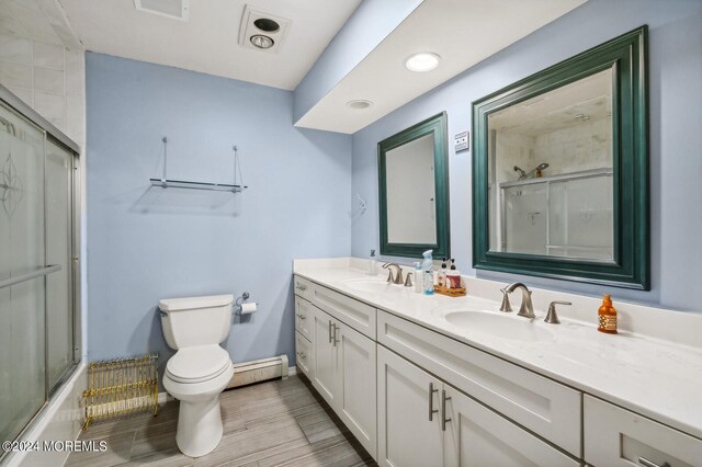 full bathroom featuring a baseboard heating unit, hardwood / wood-style flooring, shower / bath combination with glass door, toilet, and vanity