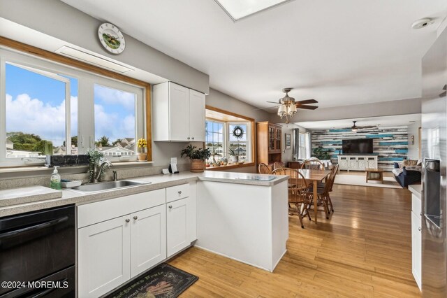 kitchen with white cabinets, black dishwasher, sink, and light wood-type flooring