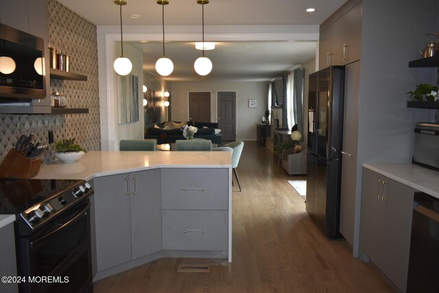 kitchen featuring hanging light fixtures, kitchen peninsula, backsplash, black appliances, and hardwood / wood-style flooring