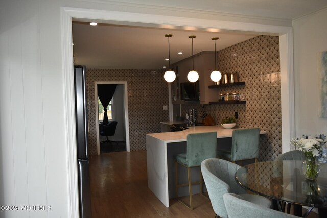 kitchen with stainless steel refrigerator, kitchen peninsula, a breakfast bar area, decorative light fixtures, and dark hardwood / wood-style floors