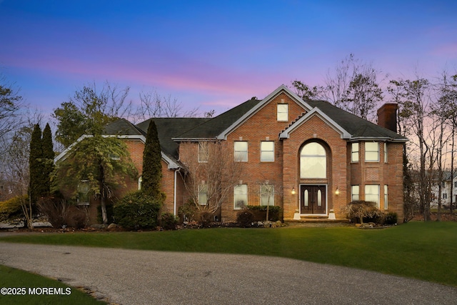 view of front of house with brick siding, a lawn, and a chimney