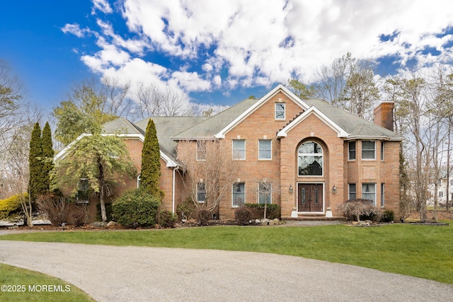 view of front of home featuring brick siding, a chimney, and a front yard