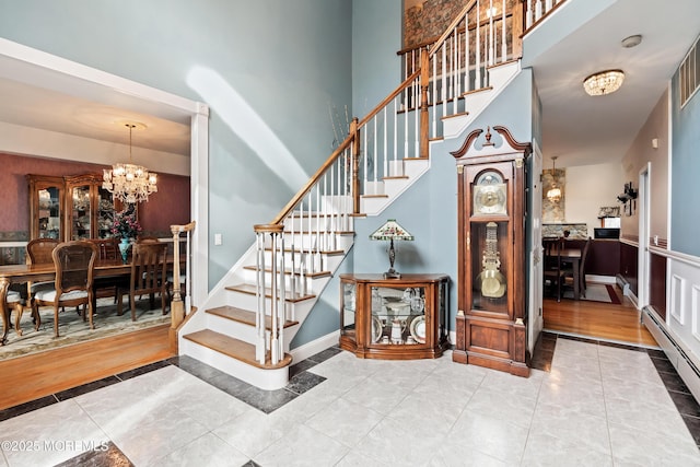 staircase featuring a baseboard heating unit, a chandelier, a towering ceiling, and tile patterned floors