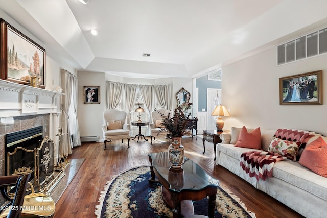 living area with a baseboard heating unit, visible vents, a fireplace, and wood finished floors