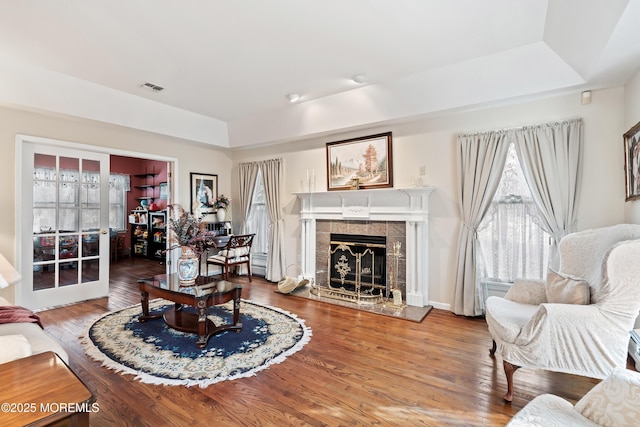 living area featuring visible vents, a raised ceiling, a tiled fireplace, wood finished floors, and french doors