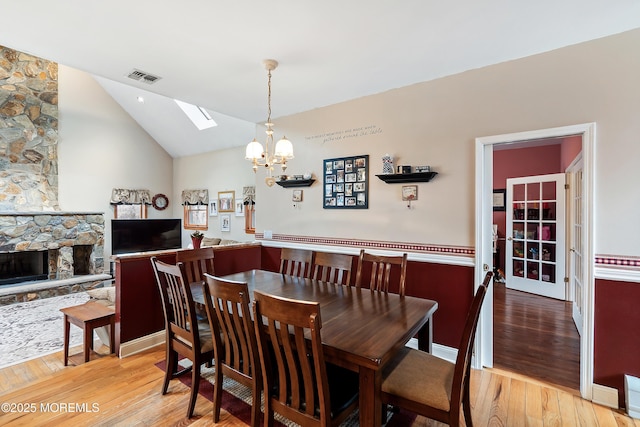 dining room featuring visible vents, lofted ceiling with skylight, light wood-type flooring, a fireplace, and a notable chandelier