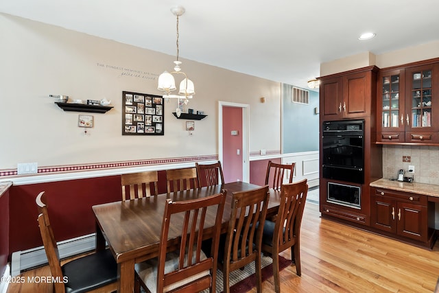 dining space with a baseboard radiator, visible vents, and light wood finished floors