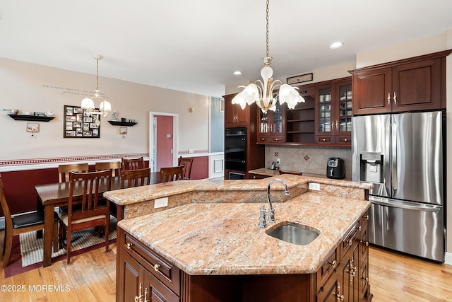 kitchen featuring a center island with sink, dobule oven black, an inviting chandelier, a sink, and stainless steel fridge