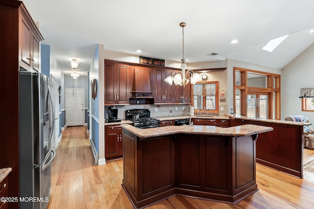 kitchen featuring stainless steel refrigerator with ice dispenser, visible vents, decorative backsplash, black gas stove, and premium range hood