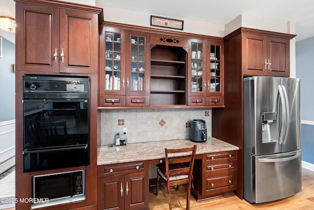 kitchen featuring light wood finished floors, tasteful backsplash, glass insert cabinets, light stone countertops, and black appliances