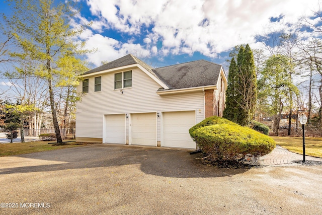 view of side of home featuring a garage, a shingled roof, fence, and aphalt driveway