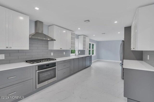 kitchen featuring white cabinetry, wall chimney exhaust hood, stainless steel appliances, decorative backsplash, and gray cabinetry