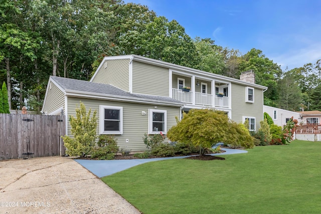 view of front of house featuring a front lawn, a balcony, fence, and a chimney