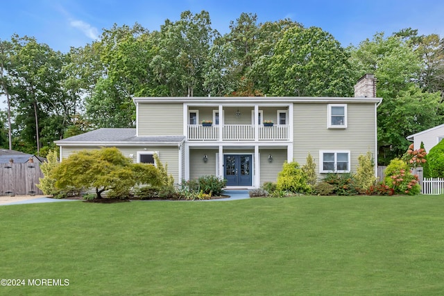 view of front of property with french doors, a front lawn, a balcony, and fence