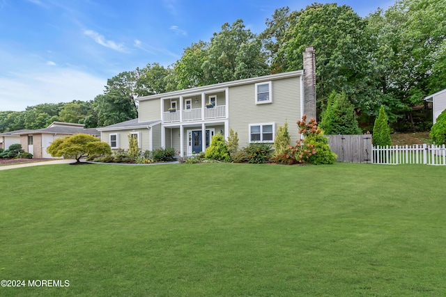 view of front of home with a balcony, a chimney, a front lawn, and fence