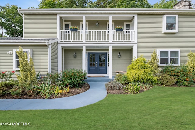 view of front of property featuring a chimney, french doors, a front lawn, and a balcony