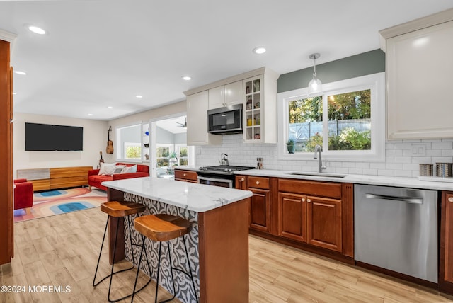 kitchen featuring glass insert cabinets, light wood-type flooring, a kitchen breakfast bar, stainless steel appliances, and a sink