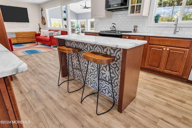 kitchen featuring decorative backsplash, appliances with stainless steel finishes, a breakfast bar area, and a healthy amount of sunlight