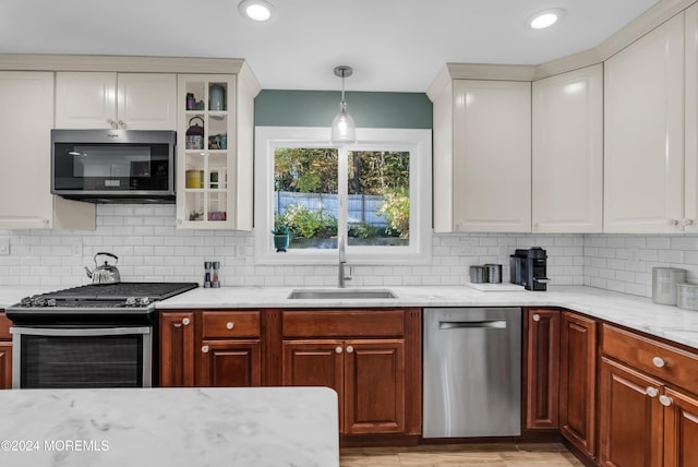 kitchen with light stone countertops, a sink, glass insert cabinets, appliances with stainless steel finishes, and tasteful backsplash