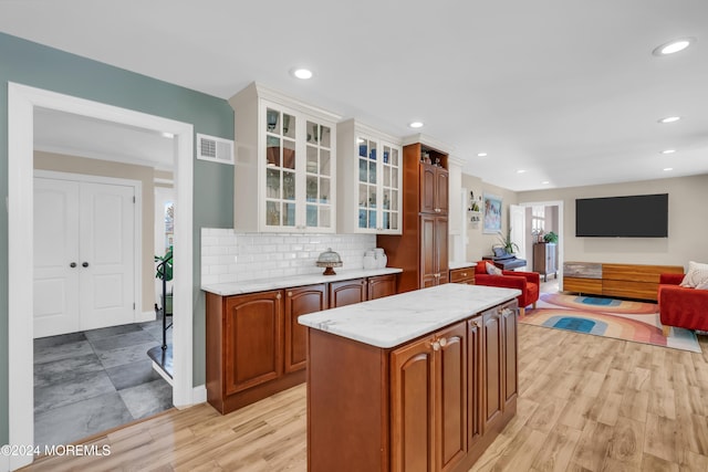 kitchen featuring visible vents, backsplash, glass insert cabinets, open floor plan, and light wood-style floors