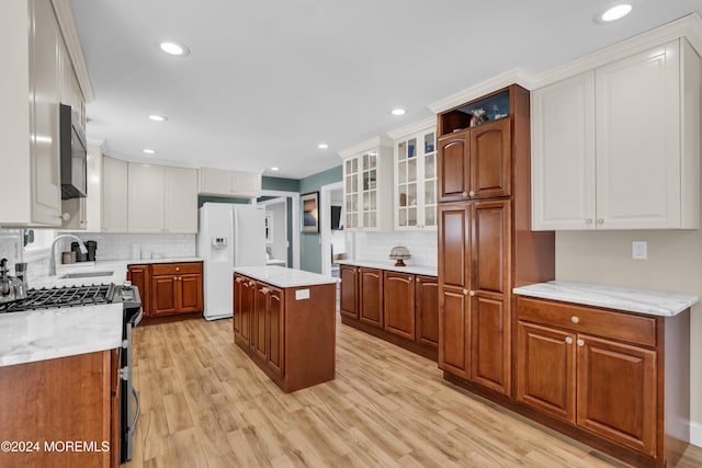 kitchen featuring light wood-style flooring, stainless steel range with gas stovetop, a sink, white fridge with ice dispenser, and white cabinetry